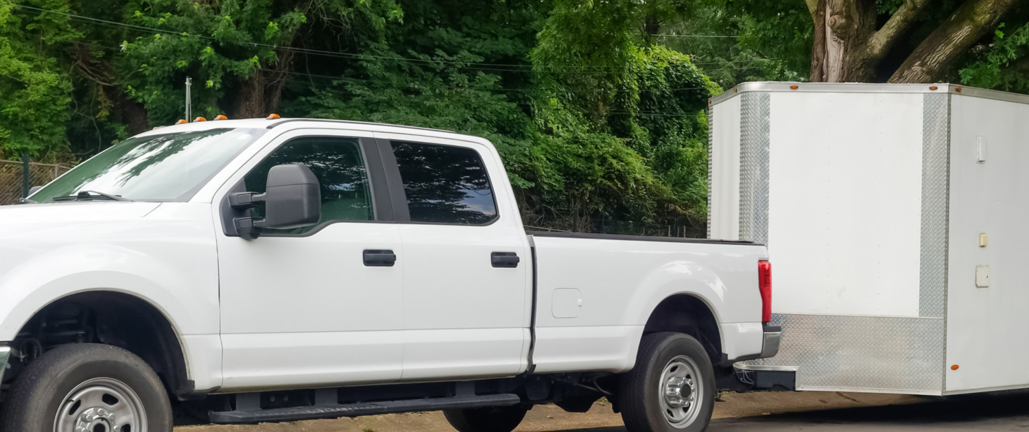 White pickup truck and large utility trailer parked on residential city street