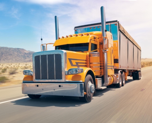 Side view of a yellow semi truck driving down the road